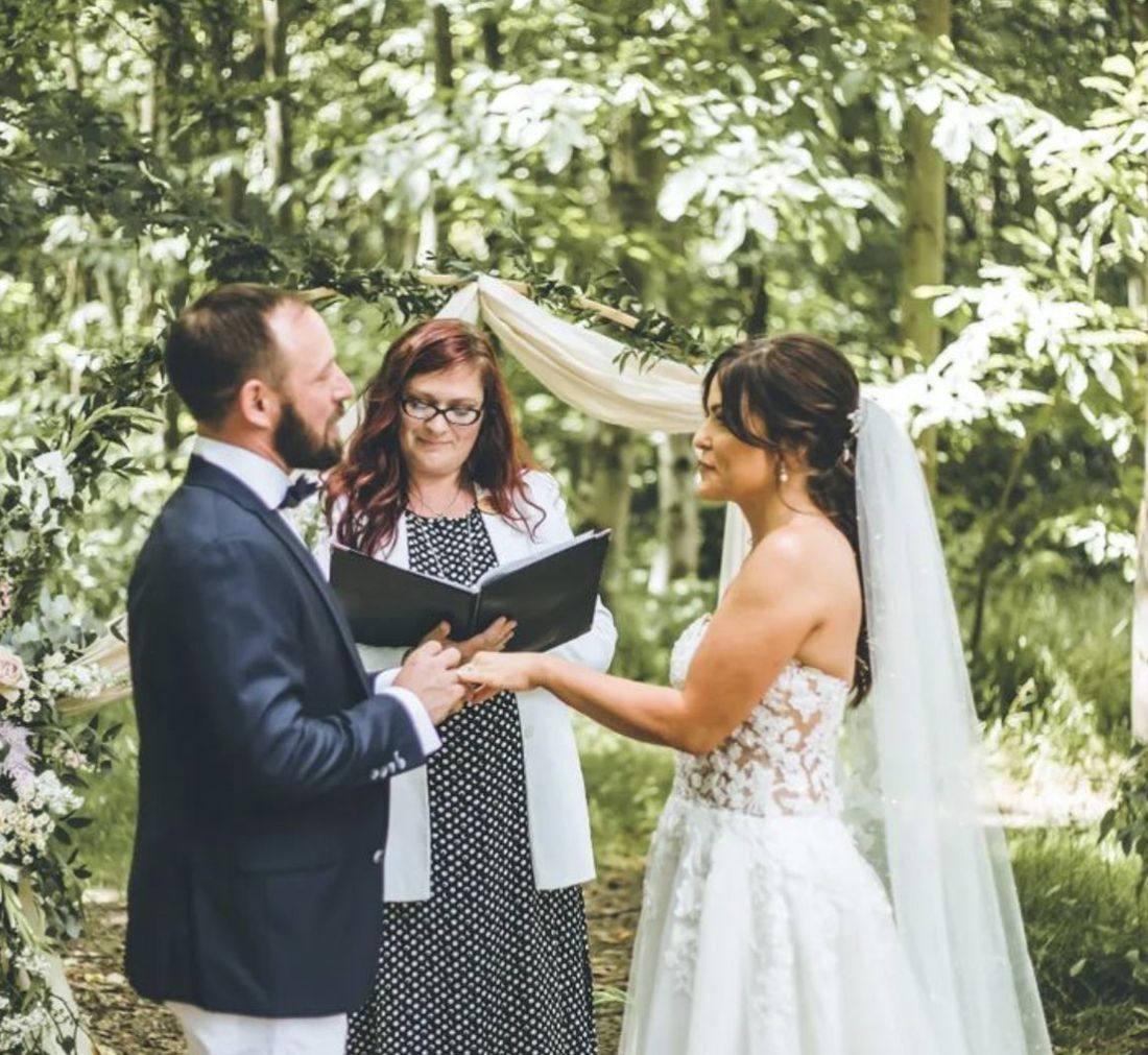 Roxanne leading a couple's vows under a woodland arch