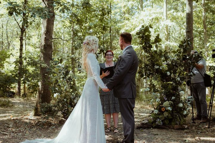 A bride and groom holding hands in a beech wood as Roxanne reads